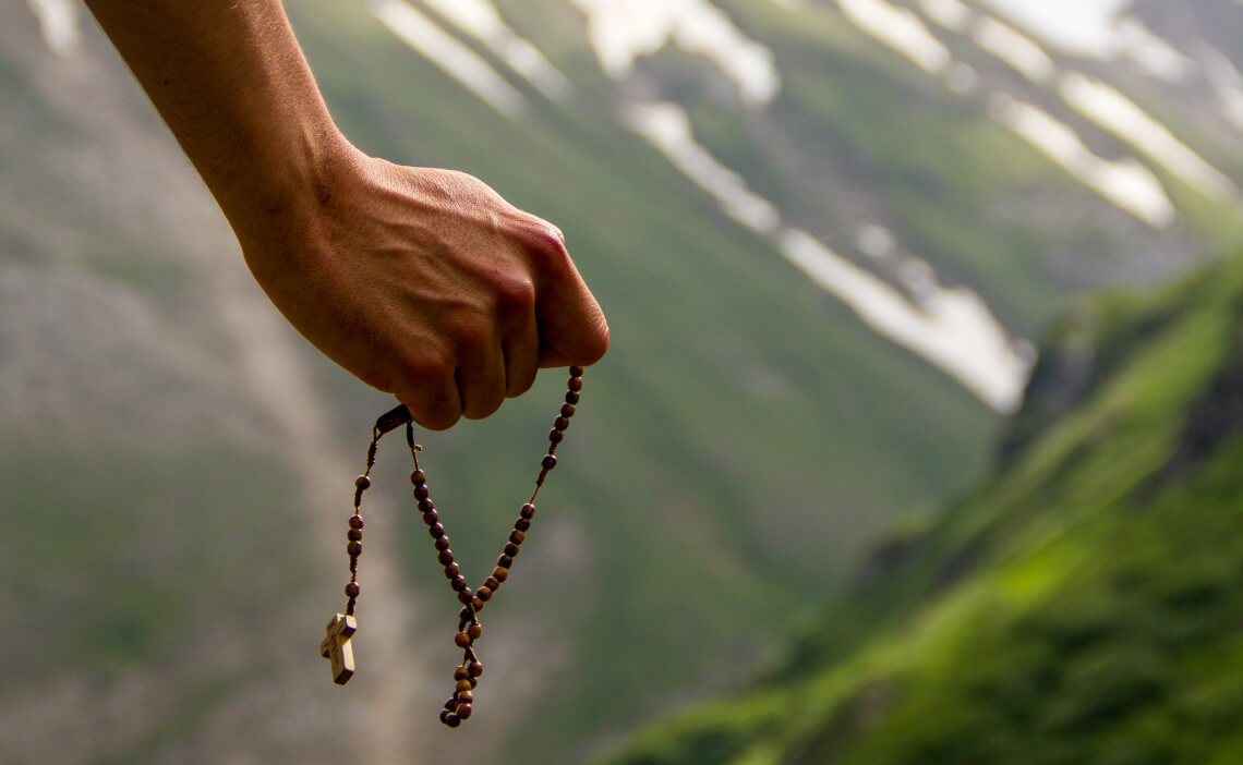 Mano sosteniendo un rosario en una montaña